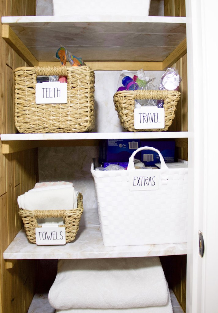 Folded towels, bins with clips for storing items inside a linen closet with marble shelf liner #organized