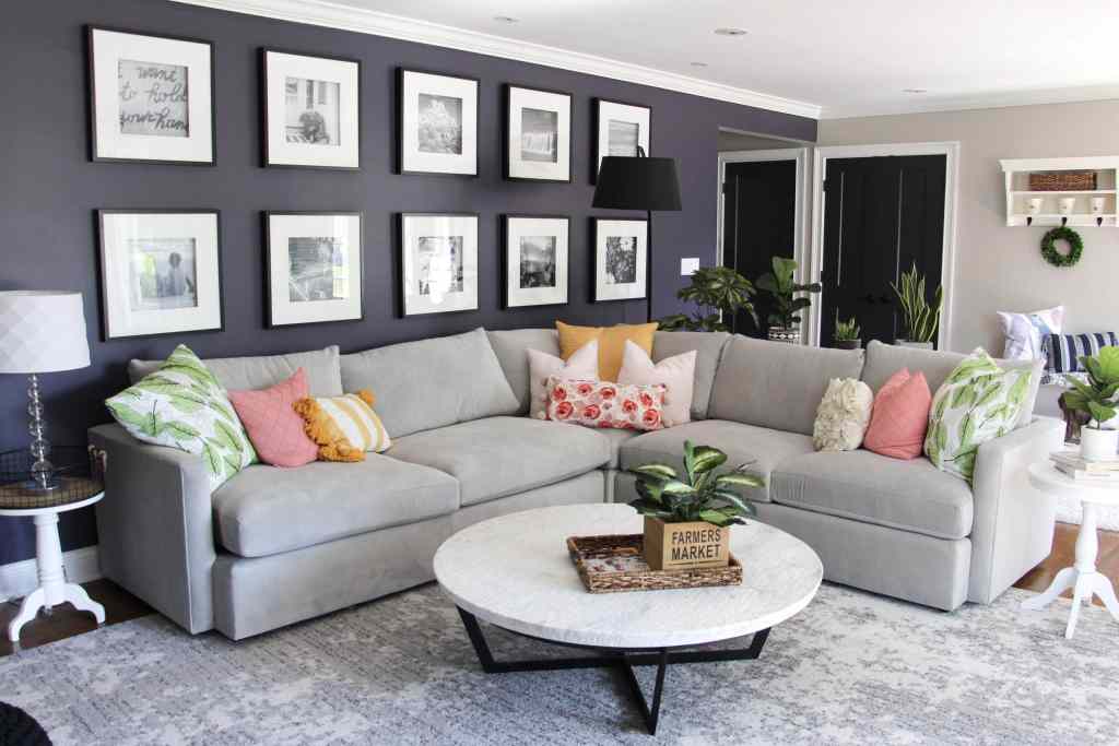 view of living room with dark purple walls, gallery wall, grey sectional with pink, green, and yellow pillows