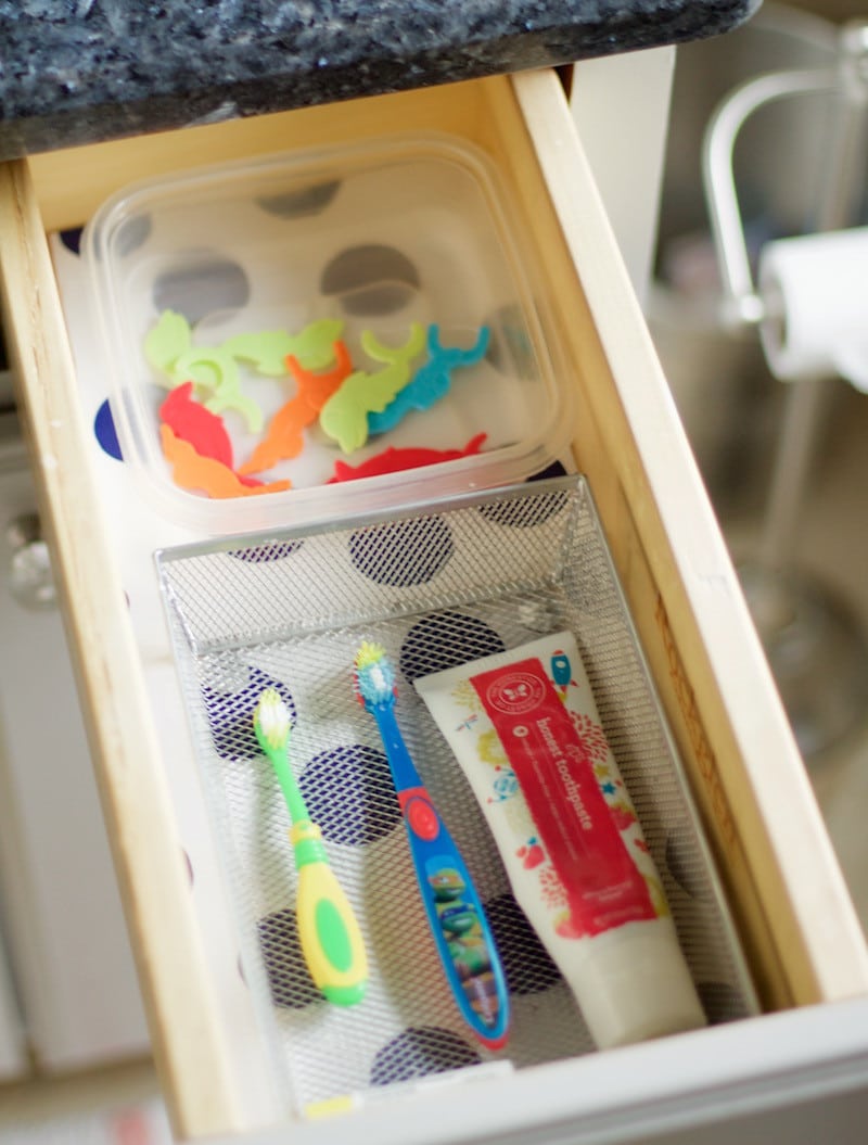 Kids' toothbrushes, toothpaste, and floss stored in small drawer with patterned liner. #bathroomorganization