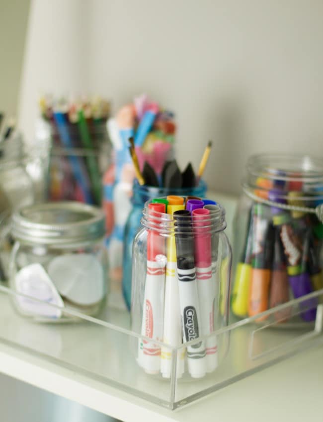 How to organize craft supplies with mason jars. Crayons are stored in mason jar, along with markers, pencils, paint brushes, and colored pencils. Embellishments are also stored and everything is contained in an acrylic tray #drawingsupplies #organization