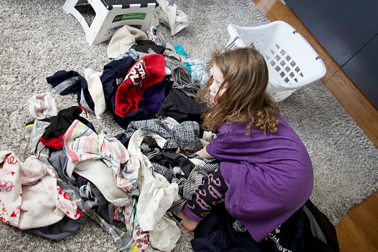 four year old sorting clothes in giant clothing pile looking for kids laundry