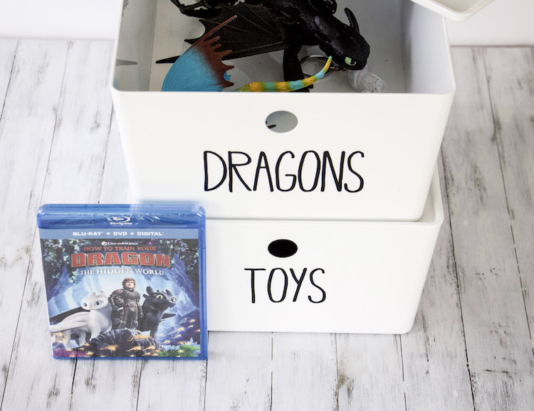 DVD of How To Train Your Dragon 3 next to two white bins with dragons from the movie inside