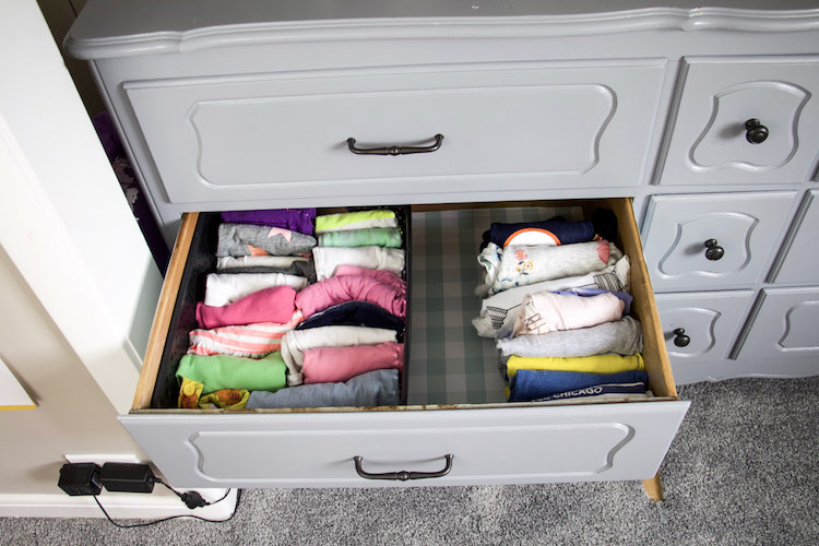 inside of a drawer with gingham drawer liner and clothing divided into t-shirts on right and tank tops on left in a container