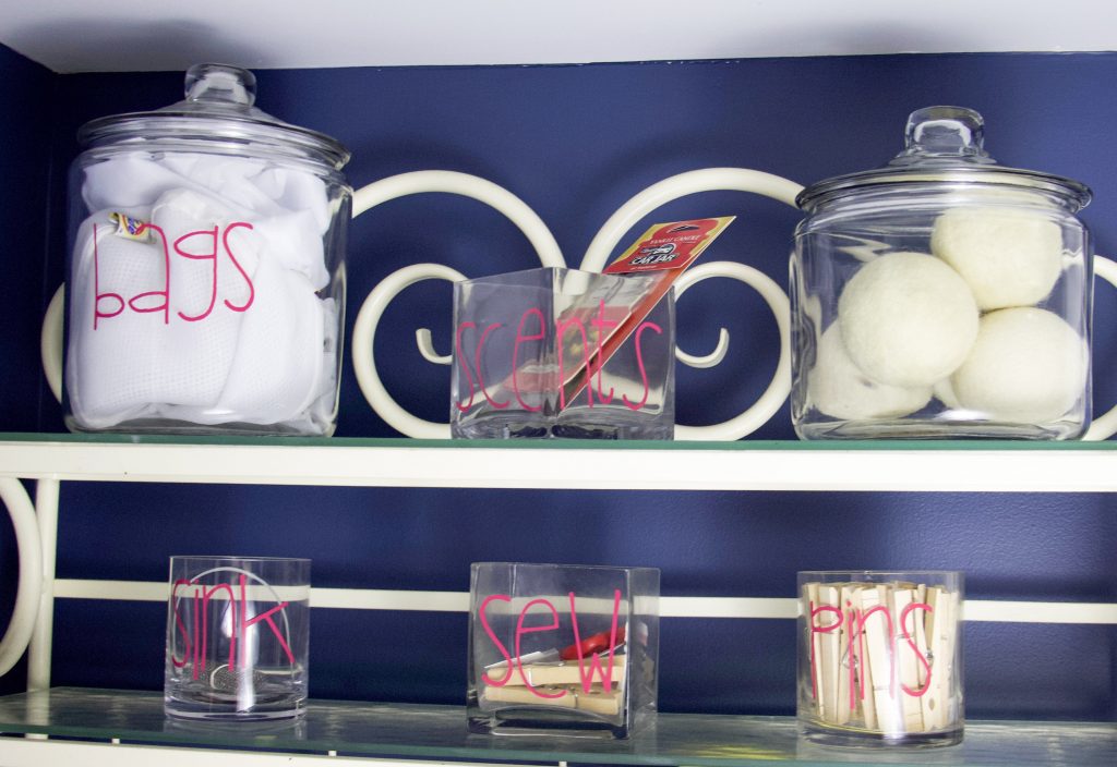 Glass jars on a bakers rack with hot pink lettering to demonstrate how to create laundry room storage in a small space