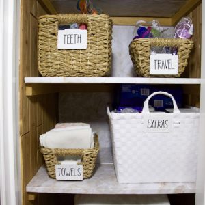 Two shelves in a linen closet with marble shelf liner and labels of extra, teeth, travel, and towels #linenclosets