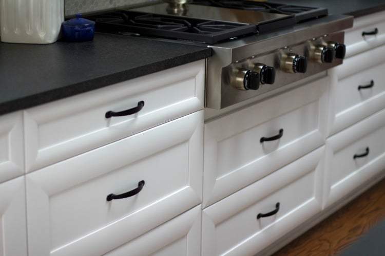 White kitchen cabinets and drawers with black countertop and hardware