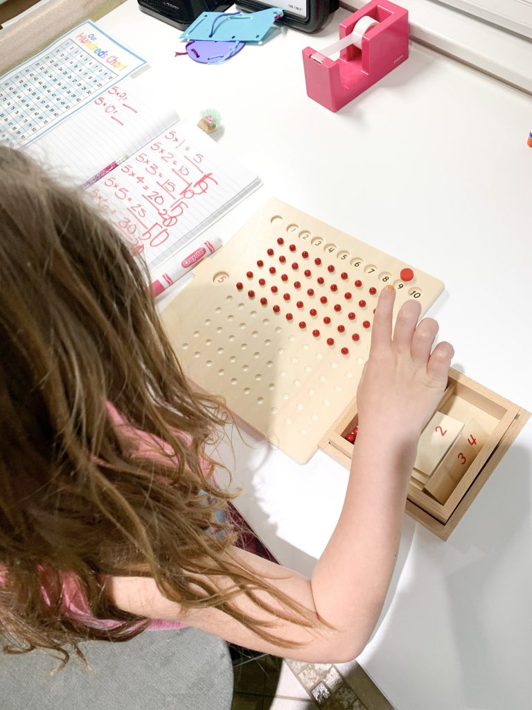 Elementary girl homeschool using manipulatives to do multiplication on bead board Montessori