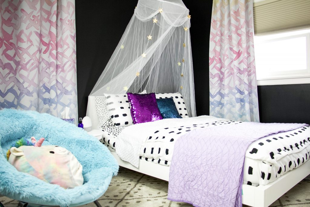 bed with white and black bedding, canopy, sparkly pillows, rug, watercolor curtains and fuzzy chair
