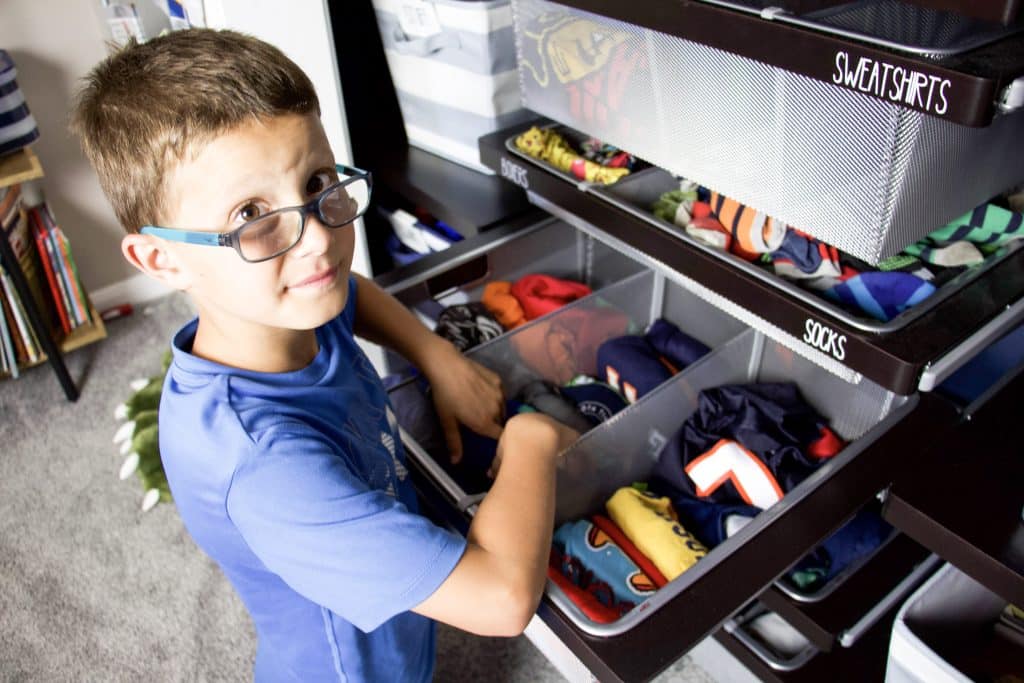boy putting clothing into closet drawers with file folded clothing