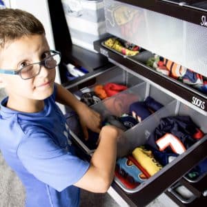 boy putting clothing into closet drawers with file folded clothing