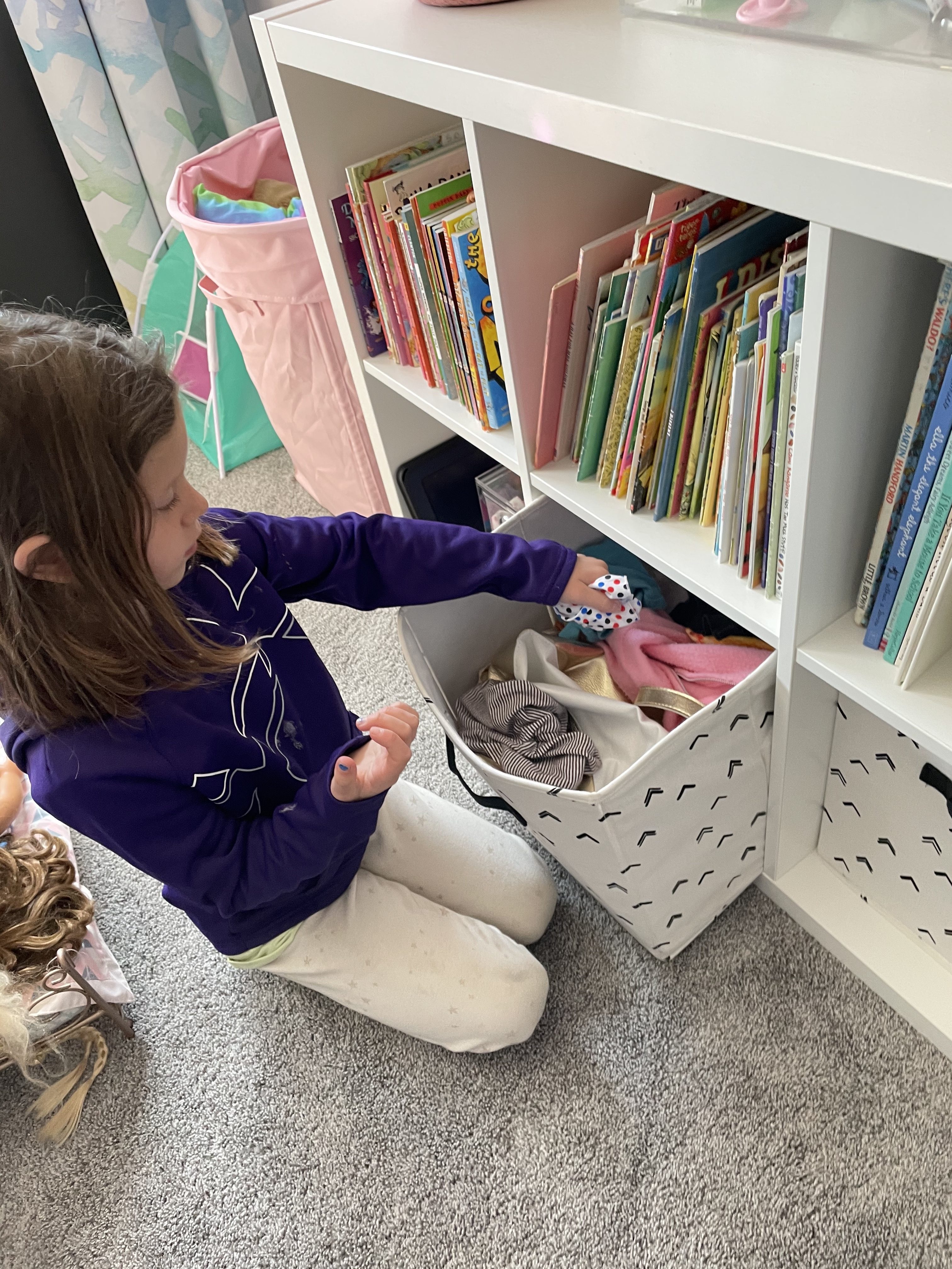 how to organize doll clothes with girl putting clothing into bin on shelf