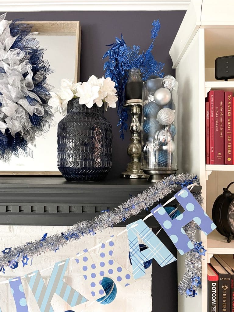 blue vase with white flowers, glass jars with blue and silver decorative balls and garland hanging from mantel
