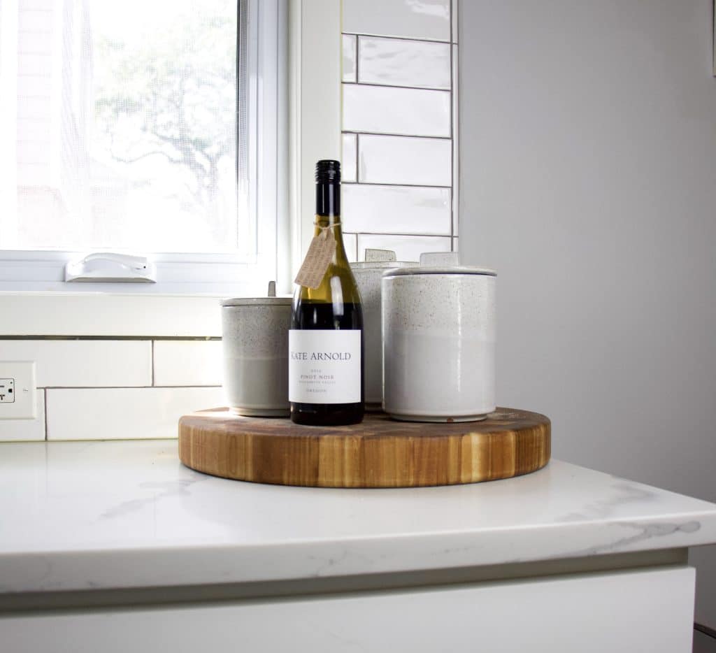 wine bottle next to canisters on cutting board in kitchen on countertop
